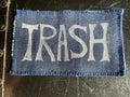 Denim patch with 'TRASH' text on a textured surface