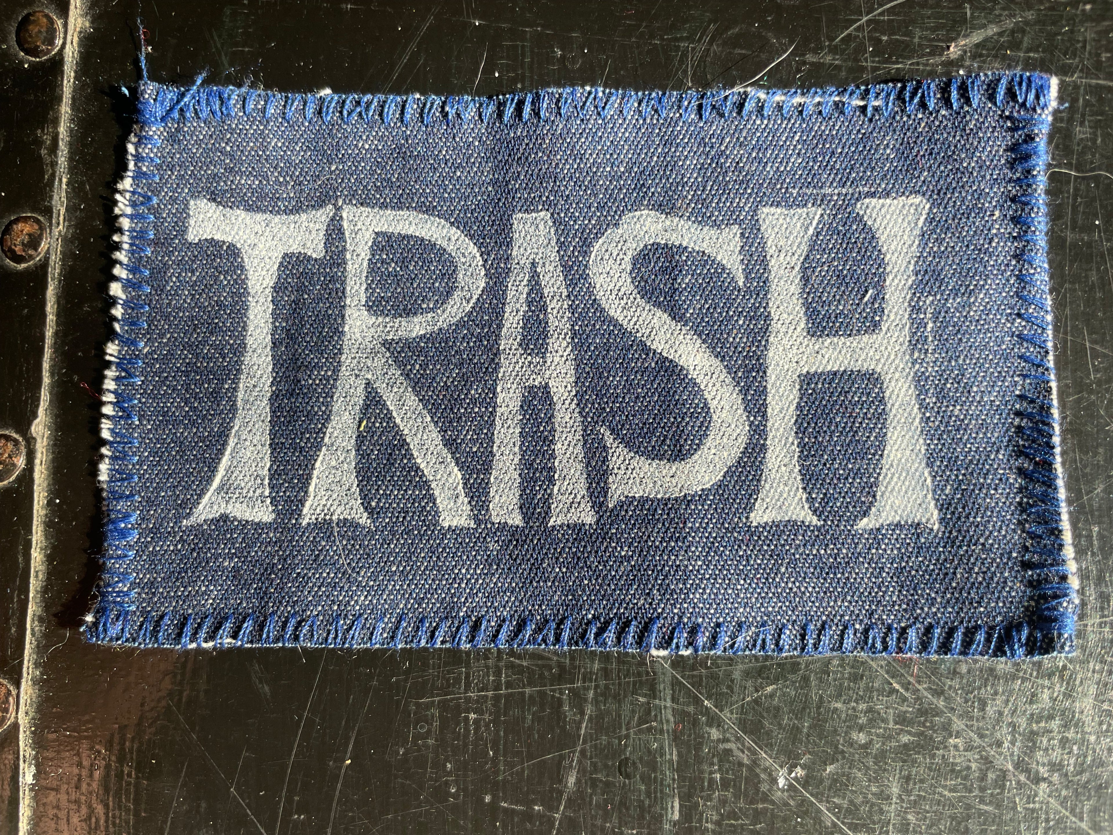 Denim patch with 'TRASH' text on a textured surface