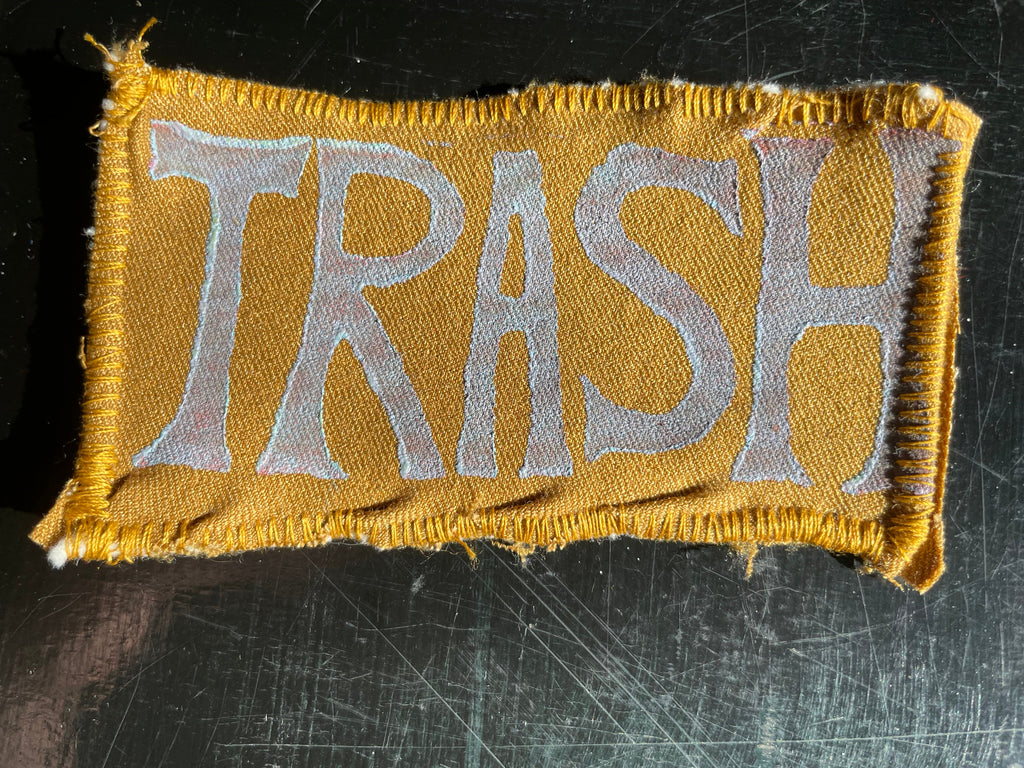 Patch with 'TRASH' text on a mustard yellow fabric