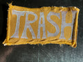 Patch with 'TRASH' text on a mustard yellow fabric