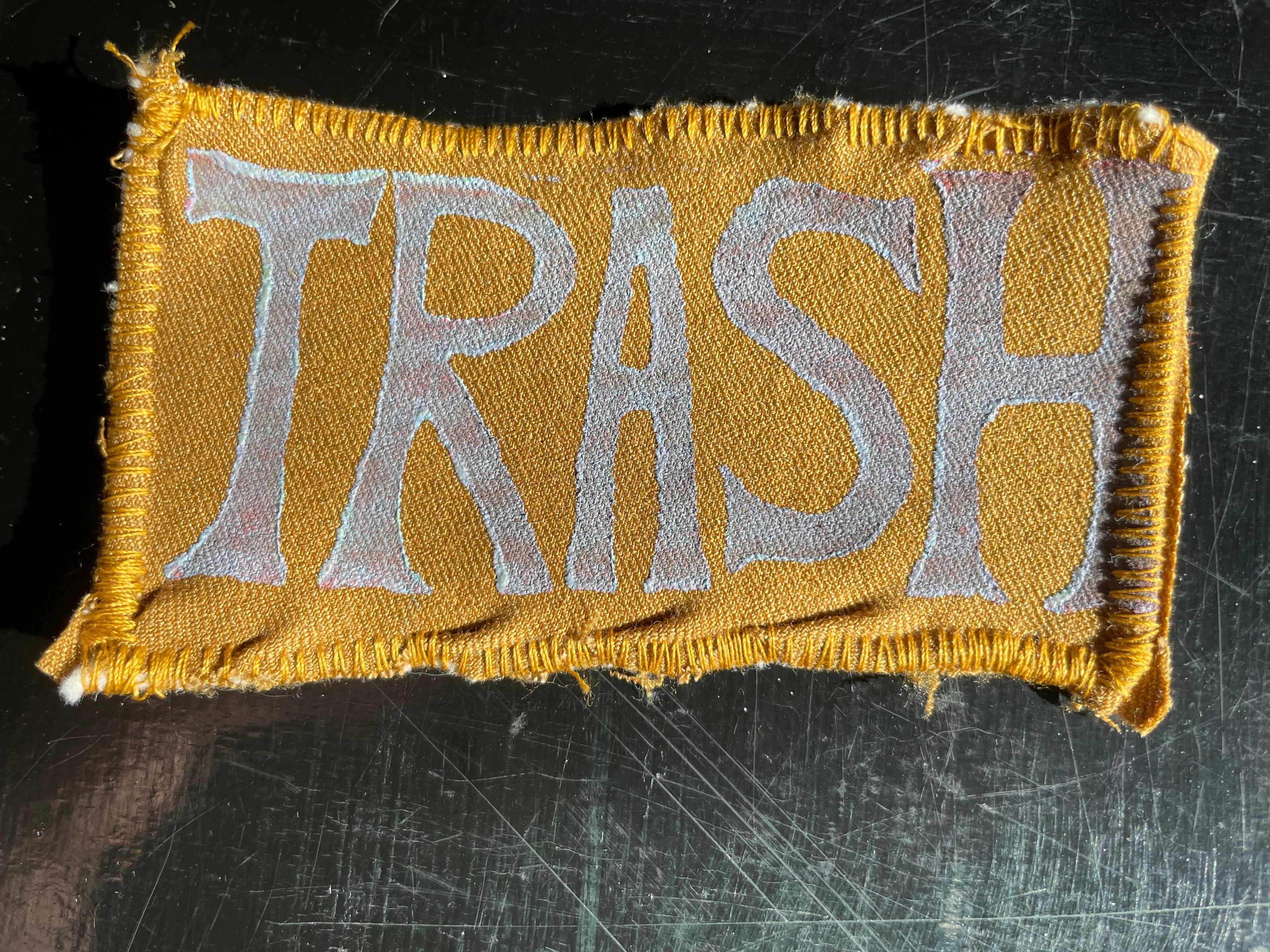Patch with 'TRASH' text on a mustard yellow fabric