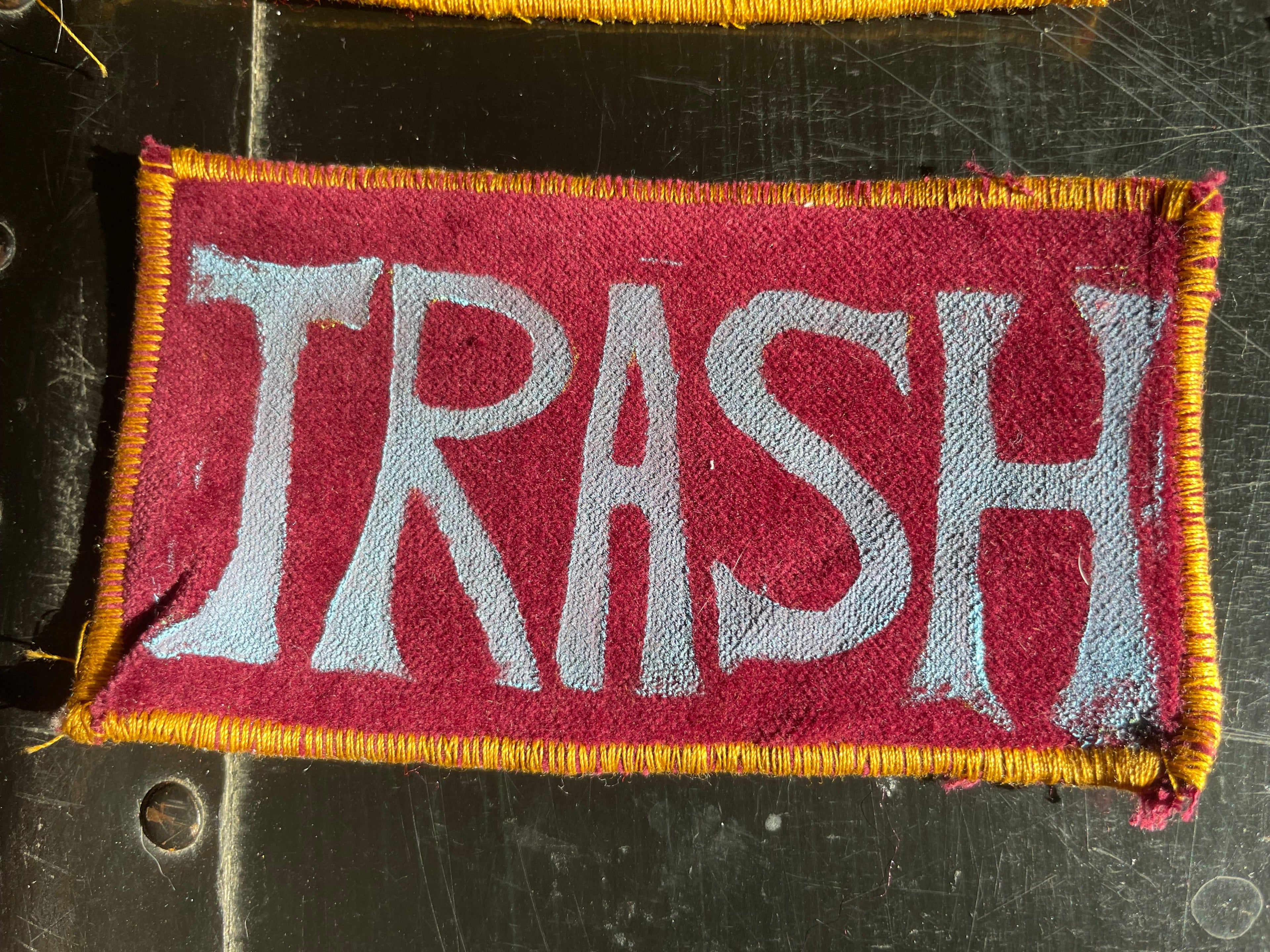 Fabric patch with 'TRASH' text on a burgundy velvet background