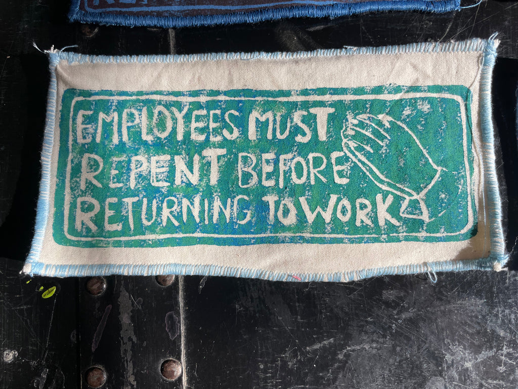 White fabric patch with text and a teal graphic on a dark background