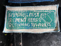 White fabric patch with text and a teal graphic on a dark background